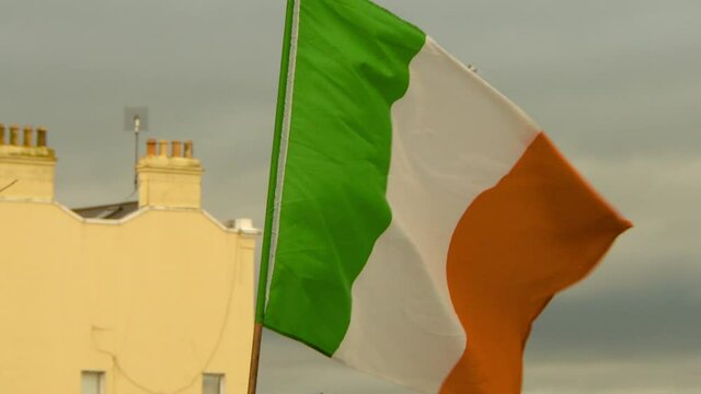 Slow motion lockdown shot of Irish flag waving in city against sky - Dublin, Ireland