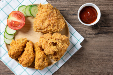 Crispy fried chicken on Round Wood plate served with cucumber, tomato and ketchup on wooden background. top view. Flat lay.