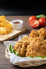 Crispy fried chicken in wicker basket serve with cucumber and potato chips on Wood cutting board serve with ketchup on wooden background.