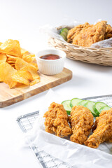 Crispy fried chicken on Sieve and wicker basket serve with cucumber and potato chips on Wood cutting board serve with ketchup on white background.