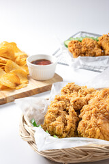 Crispy fried chicken on Sieve and wicker basket serve with cucumber and potato chips on Wood cutting board serve with ketchup on white background.