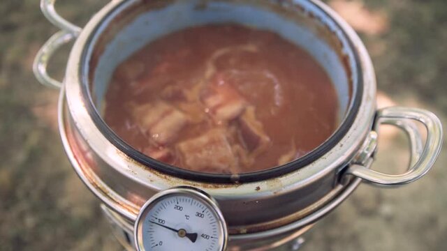 Red beans boiling next to condiments cooked in a traditional pot with handles, also called "putxera" or "puchera" with a built-in kitchen thermometer