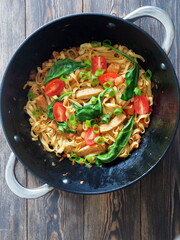 Stir fried noodles with turkey meat and fresh spinach and vegetables in an iron wok pan. Chinese cuisine.