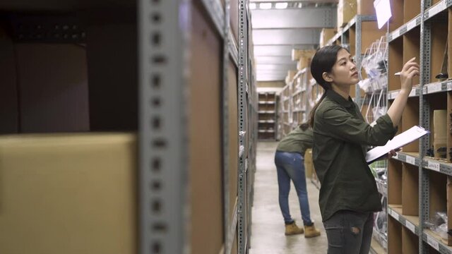 two asian japanese women worker stock taking in big warehouse. group of beautiful young female coworkers of furniture store in uniform and holding clipboard and tablet counting products in stockroom