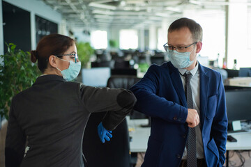 Two colleagues avoid a handshake when meeting in the office and greet bumping elbows. Greetings in Wuhan. A man and a woman in medical masks maintain a social distance at work.