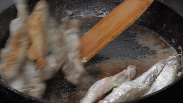 Cooking frying and stirring capelin fish fried in iron pan. Close-up view of chef stirs roasted caplin fish with wooden spatula. Grilled fish tasty delicious Chinese cuisine as an appetizer or garnish