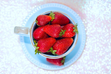 Sweet strawberries in a blue ceramic Cup with a saucer on a shiny background