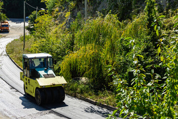 Tuapse, Russia - September 14, 2019: An asphalt compactor is working on laying asphalt in mountainous area. Close-up. Asphalt is laid on concrete road leading to mountains. Road works.