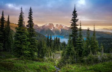 Glacial mountain Garibaldi lake with turquoise water in the middle of coniferous forest at sunset....