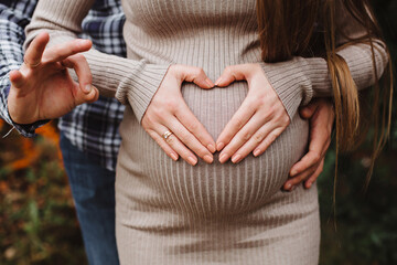 Heart of hands by multiethnic couple on pregnant belly. Man holding belly of his pregnant wife making heart. Pregnant woman and loving husband hugging.