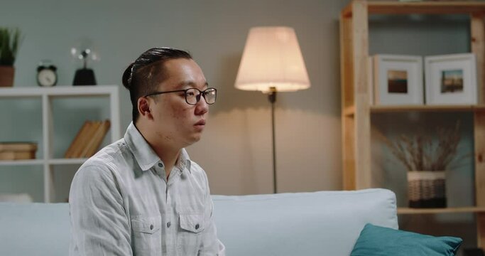 Sick young asian man sitting at home and coughing because he is infected with flu, then putting on black mask - coronavirus, desease carrier concept 4k footage