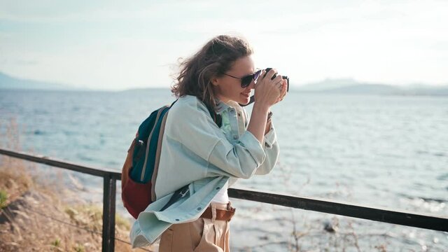 Happy young woman takes a picture on a photo camera walking sea, summer travel. High quality 4k footage