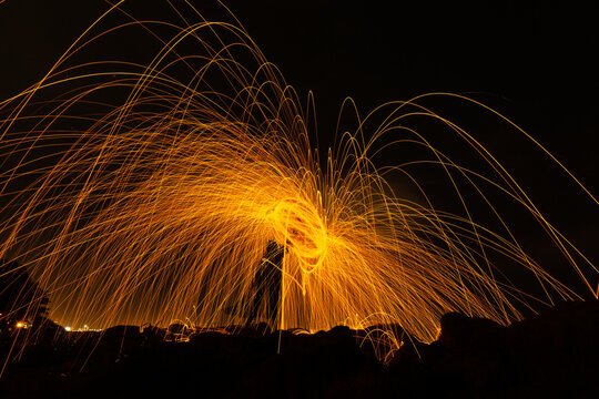 The silhouette of a person is spinning spiral sparks on the rocks at night capture with a long exposure. Stunning light painting in fountain form.