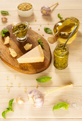 Homemade traditional pesto sauce: basil, olive oil, parmesan, garlic, pine nuts.  Ingredients lay on brown wooden board and on light wooden table. Top view. Vertical.