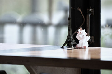A unicorn doll put on wood table belong with an Eiffel Tower model put in front of a handle of window with sunshine on morning time