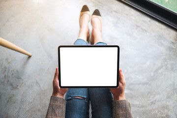 Top view mockup image of a woman holding and using tablet pc with blank white desktop screen while sitting on the floor