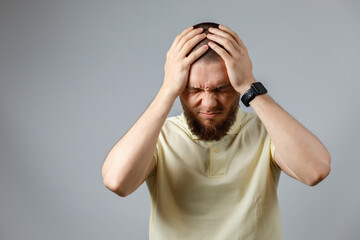 Portrait of a young upset man in a yellow t-shirt holding his head on a gray background. isolated. copyspace