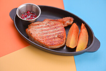 Rib eye steak served with baked potatoes and cranberry sauce on a black tray over light colorful background.