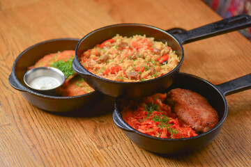 Delicious potato pancakes with sour cream, rice with meat and vegetables and Chicken Kiev cutlet served in frying pans.