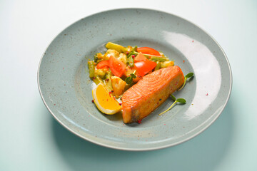 Baked salmon steak with healthy vegetable salad. Organic delicious dinner served on a blue plate over blue background.