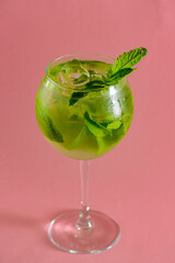 Mojito alcohol cocktail, tropical beverage with ice, mint and lime on pastel pink background with copy space.