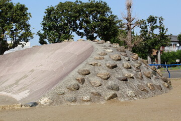 A Japanese neighborhood park with a stone-studded concrete mound for climbing and a slope with a...