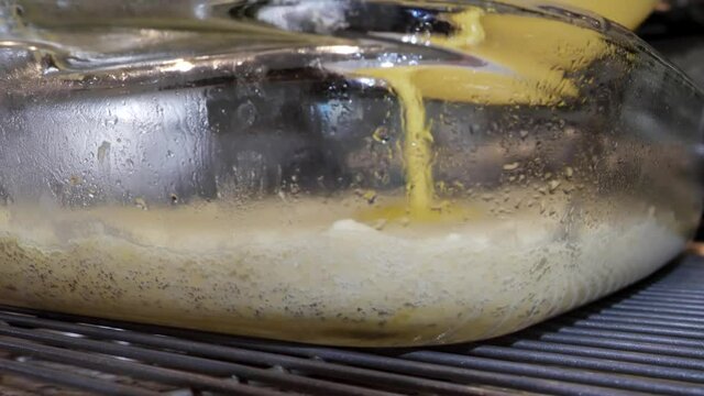 Pouring lemon mix in glass dish over shortbread crust, making lemon bars