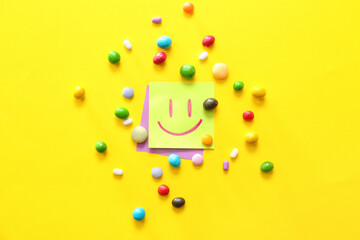 Papers with drawn happy face and candies on color background