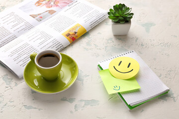 Notebook with paper smile, cup of coffee and newspaper on light background