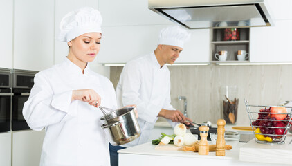 Portrait of woman cook who is standing with pot for soup on her work place in the kitchen