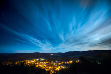 High angle view over the town Zell in Germany, Bavaria, Upper Palatinate at night with starry sky and clouds