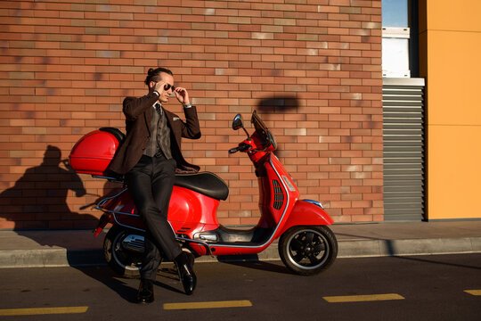 Youman man in elegant suit is leaning on a red vintage scooter motorbike