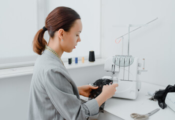 Young woman tailor is looking at a piece of black material in her white mini workshop and preparing...