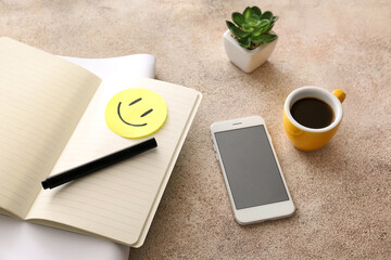 Notebooks with paper smile, mobile phone and cup of coffee on grey background