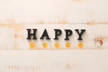 Word HAPPY and paper smiles on white wooden background