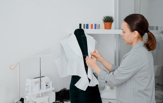 Young woman tailor is arranging a future shirt on a mannequin in her mini workshop.