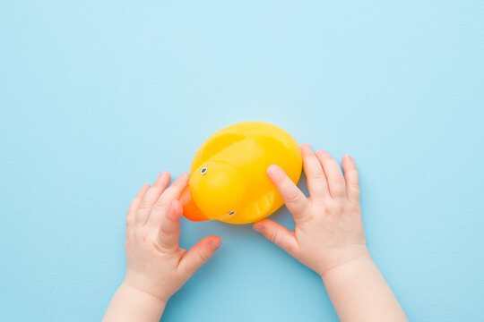 Baby hands touching yellow rubber duckling on light blue table background. Pastel color. Closeup. Bathing toy for little kids. Point of view shot. Top down view.