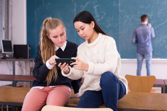 Cheerful teen girls with phone in classroom