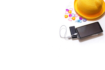 Smartphone on an external battery charge next to beach accessories: yellow straw hat, seashells,...
