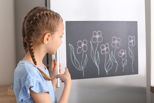 Little girl near chalkboard on refrigerator in kitchen