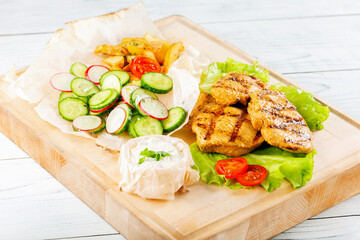 Grilled chiken fillet on wooden board with vegetables. Delicious roasted turkey breast.