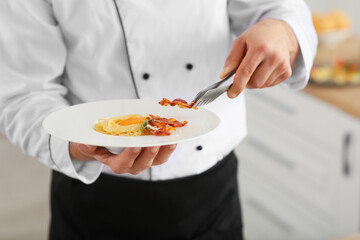 Handsome male chef with tasty pasta carbonara in kitchen, closeup