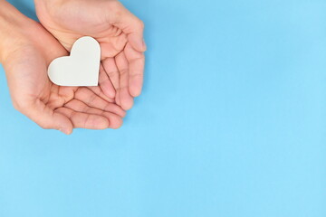 Cupped hands holding a white heart in blue background. Charity, pure love, compassion and kindness...