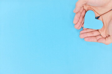 Cupped hands holding a blue heart in blue background. Charity, pure love, compassion and kindness...