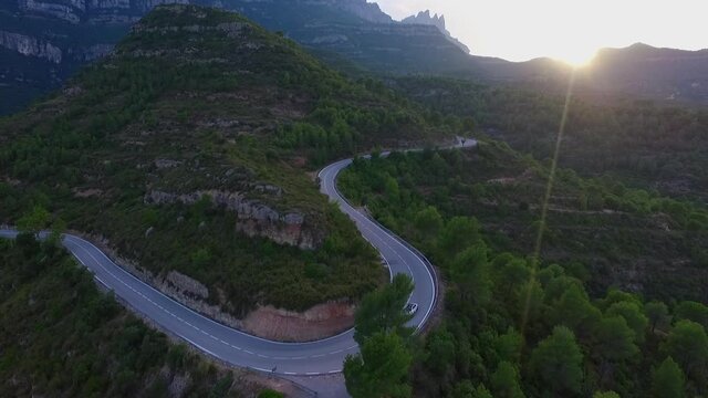 Aerial shot of car on road amidst green trees and plants, drone flying forward over natural landscape during sunset - Montserrat, Spain