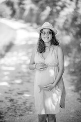 Outdoor portrait of happy pregnant woman with sunglasses and hat - summer time in nature - beautiful moments of family life