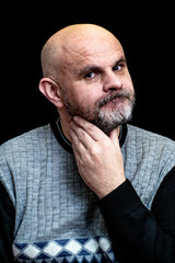 black man with gray beard on the black background scratches his beard with his hand