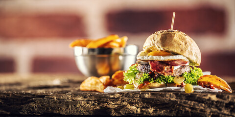 Beef burger with fried egg, bacon, lettuce, potato wedges and grapes on a rustic wood