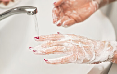Fototapeta premium Young woman washing her hands under water tap faucet with soap. Detail on suds covered skin. Personal hygiene concept