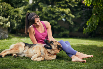 Young attractive fit yogi brunette playing with her dog in backyard.
